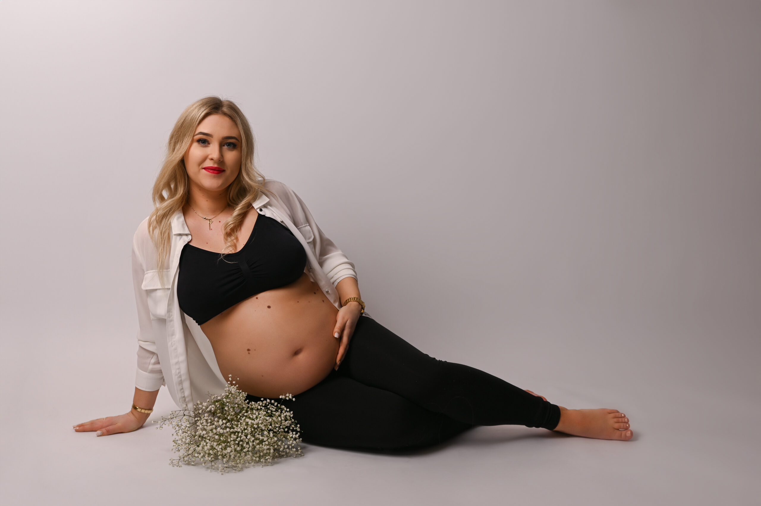 kobieta w ciąży siedząca na podłosze z bukietem gipsówki