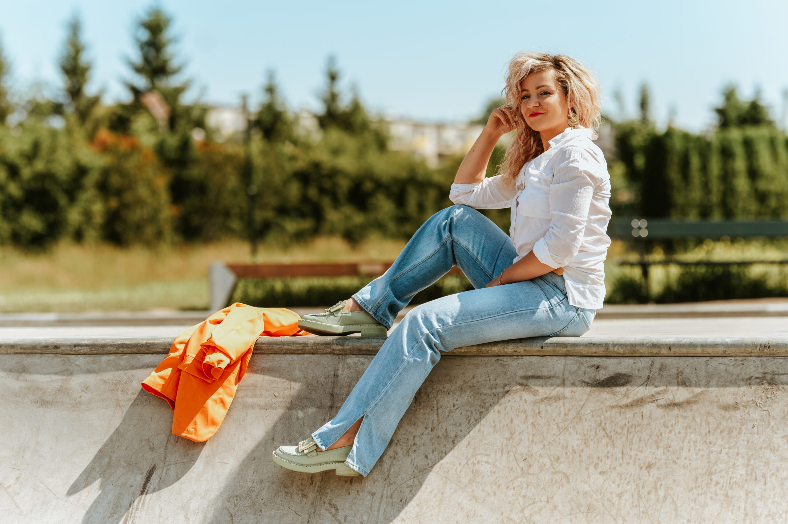 kobieta ubrana w koszulę i jeansy siedząca na skateparku