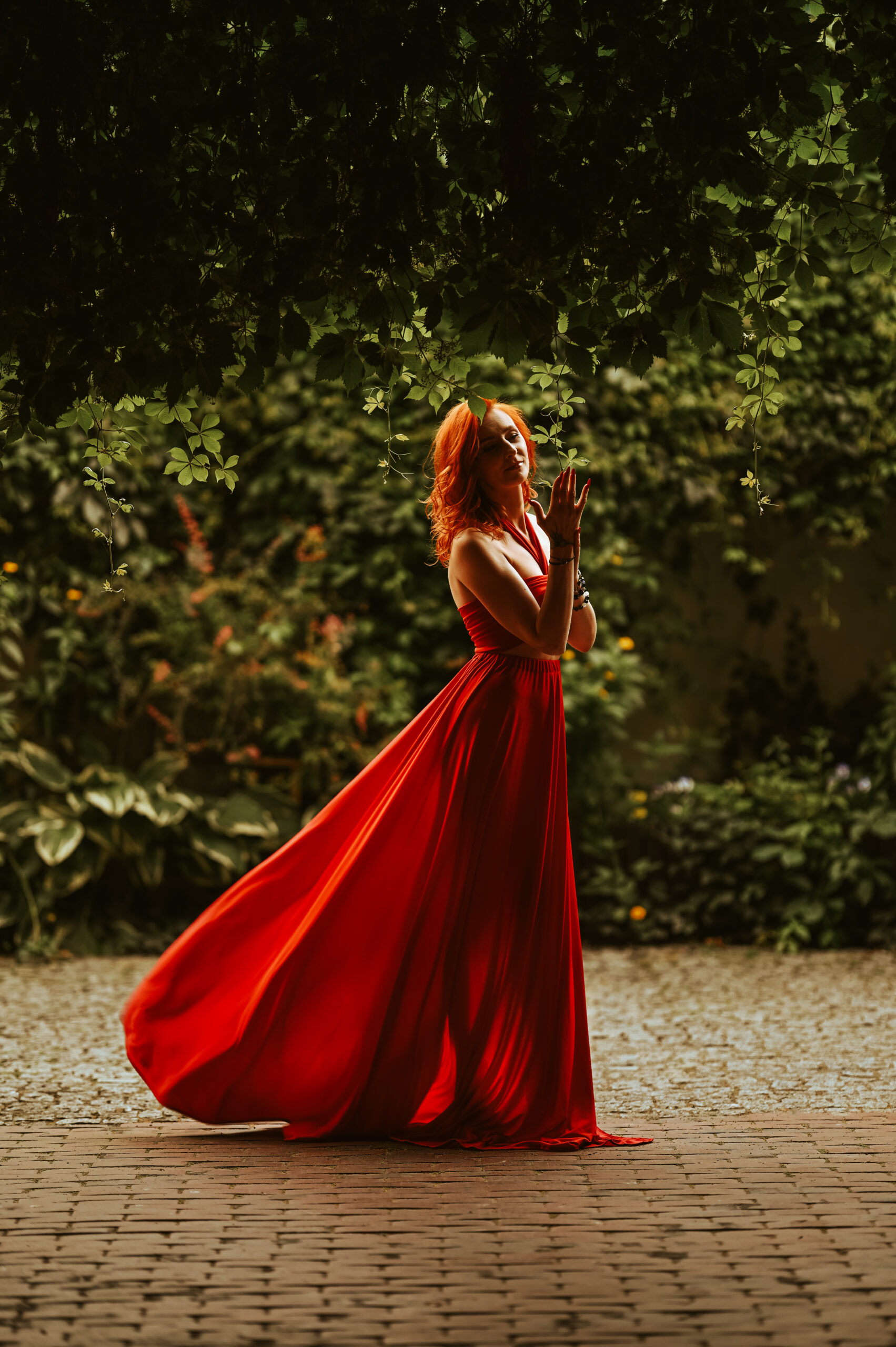 kobieta w czerwonej sukience między zielonymi zaroślami