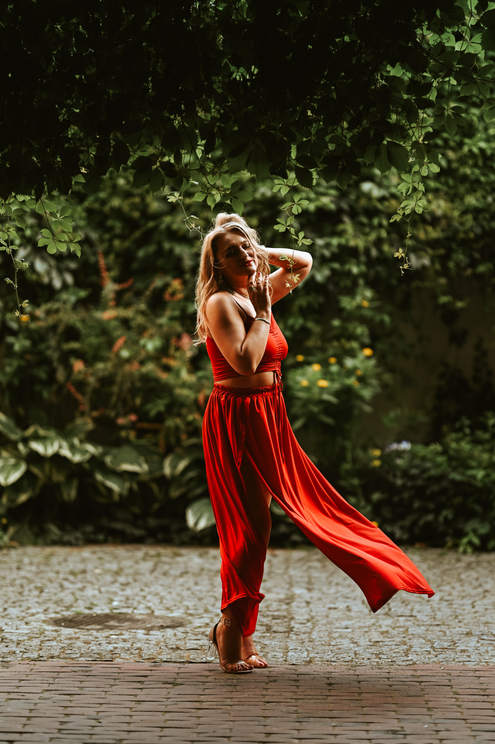 kobieta w czerwonej sukience stojąca pośród zielonych zarośli