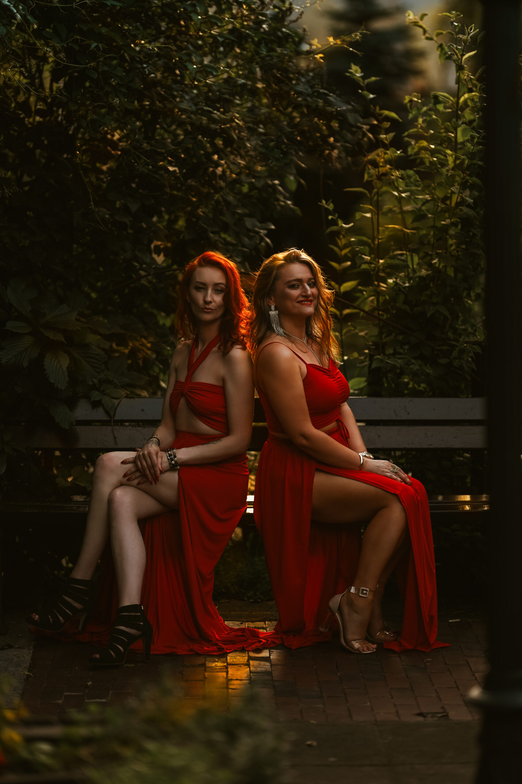 dwie piękne kobiety siedzące na ławce w czerwonych sukienkach