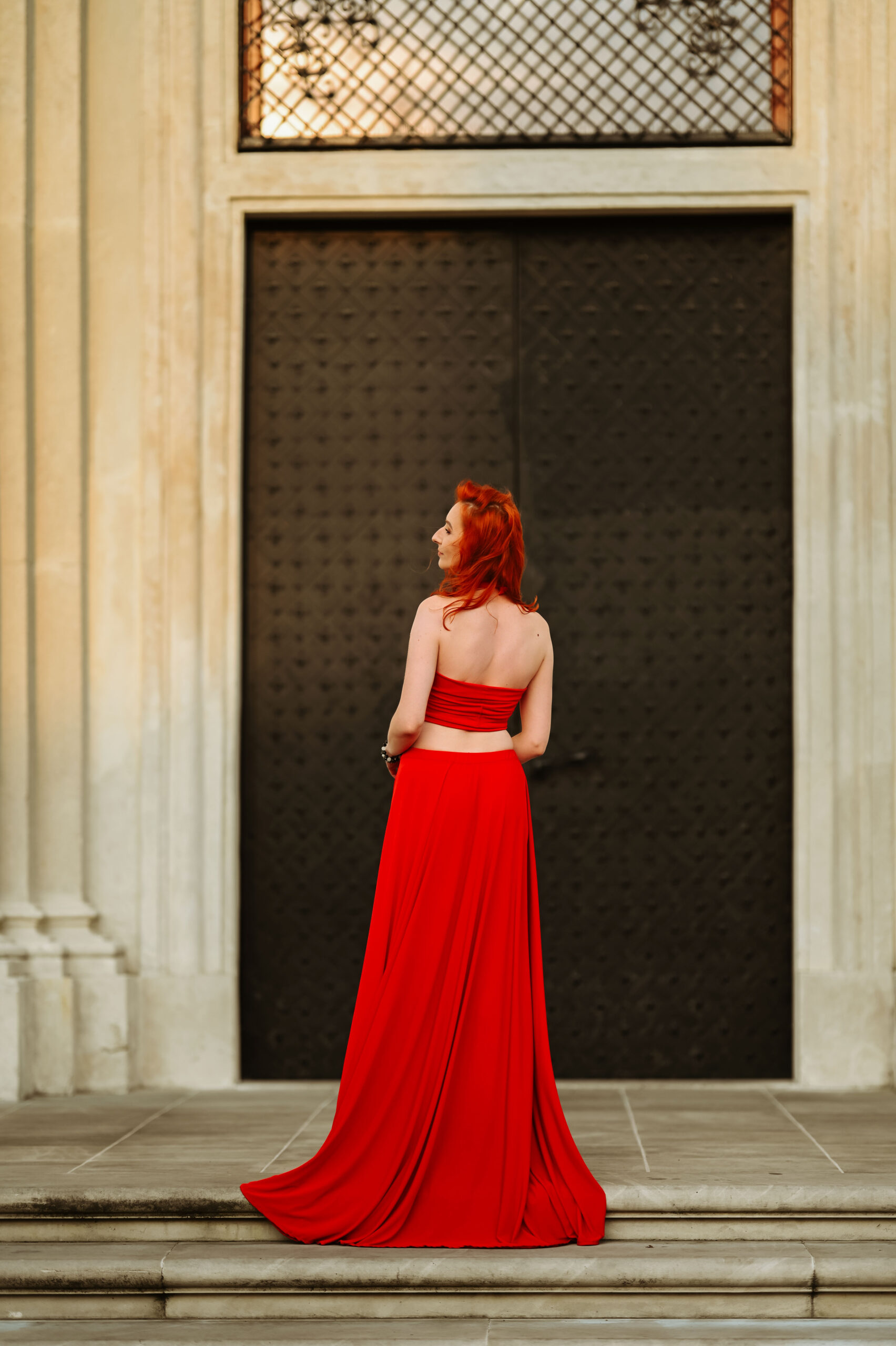 kobieta w czerwonej sukni stojąca na zabytkowych schodach