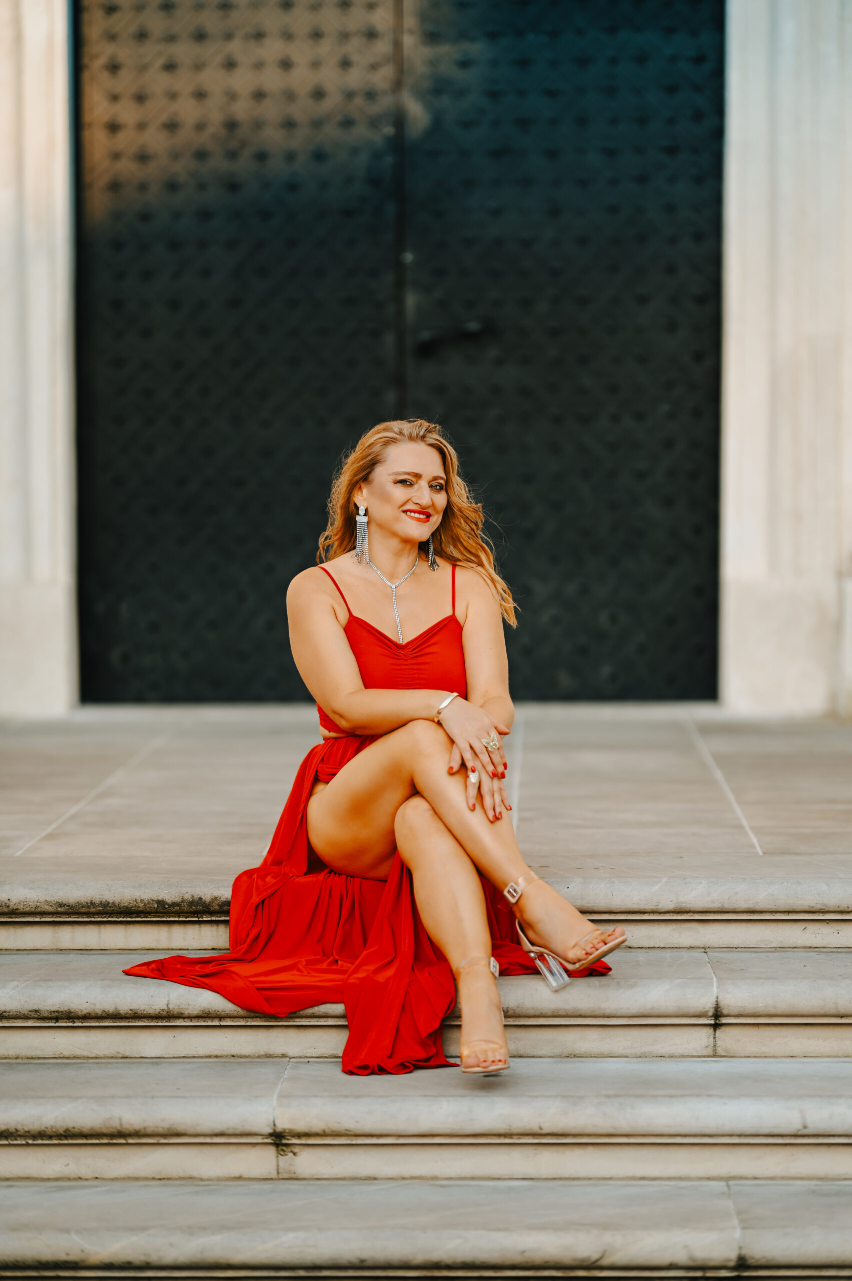 kobieta w czerwonej sukience siedząca na zabytkowych schodach