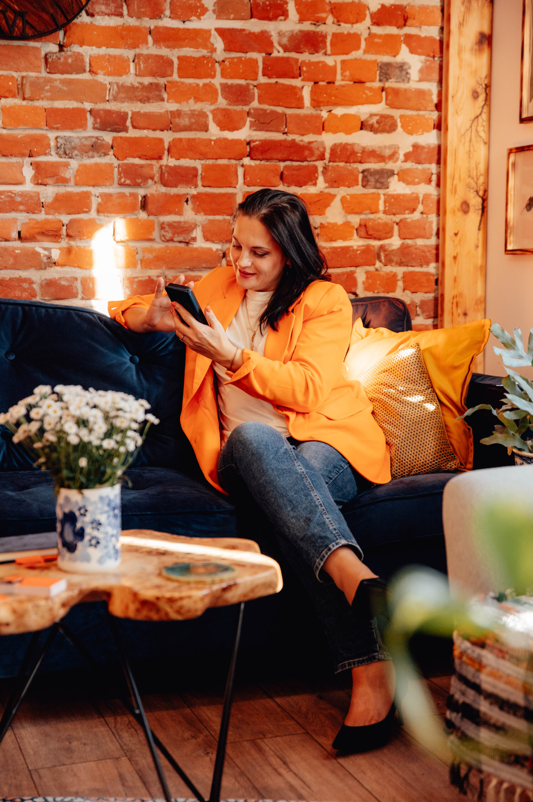 kobieta bizneswoman w pomarańczowym garniturze siedząna na niebieskiej kanapie obok cegieł